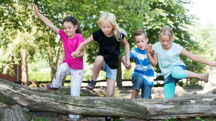 Auch Sport- und Outdoor-Aktivitäten kommen beim Englisch-Camp nicht zu kurz. © Christian Schwier, stock.adobe.com Kinder springen Hand in Hand über Baumstamm