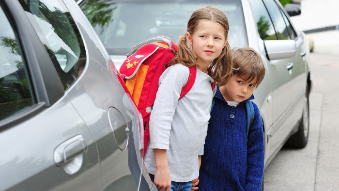 Zwei Schulkinder stehen zwischen Autos auf der Straße.