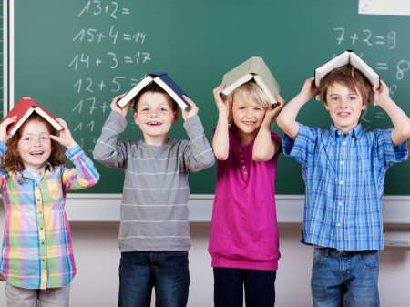 Kinder vor der Tafel mit Büchern am Kopf